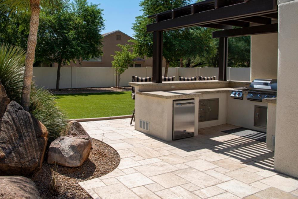 A patio with a grill and a dishwasher under a pergola.