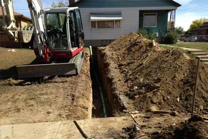 A red mini excavator digs a trench in a residential yard near a house.