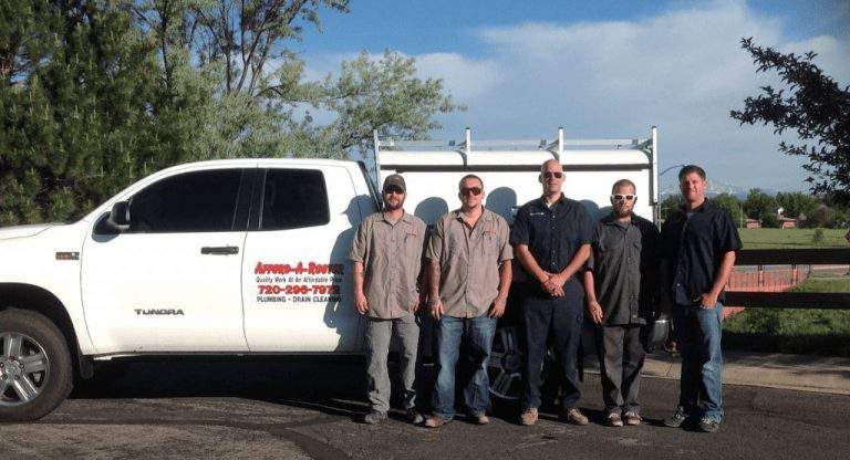 Five men in work uniforms stand in front of a white utility truck on a sunny day.
