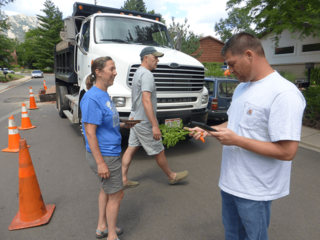 Two people talk in a residential street near a parked white dump truck and orange traffic cones.