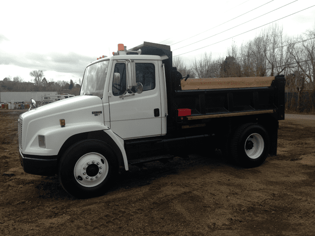 A white dump truck parked on a dirt lot under an overcast sky.