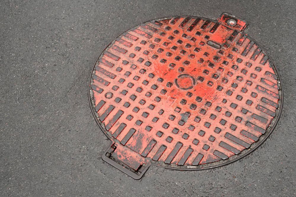 A round, bright red metal manhole cover with a grid pattern, set into gray asphalt.