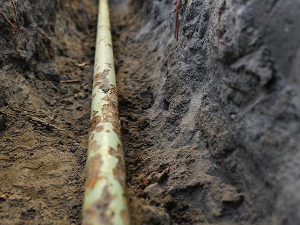 A green pipe is laying in the dirt in a trench.