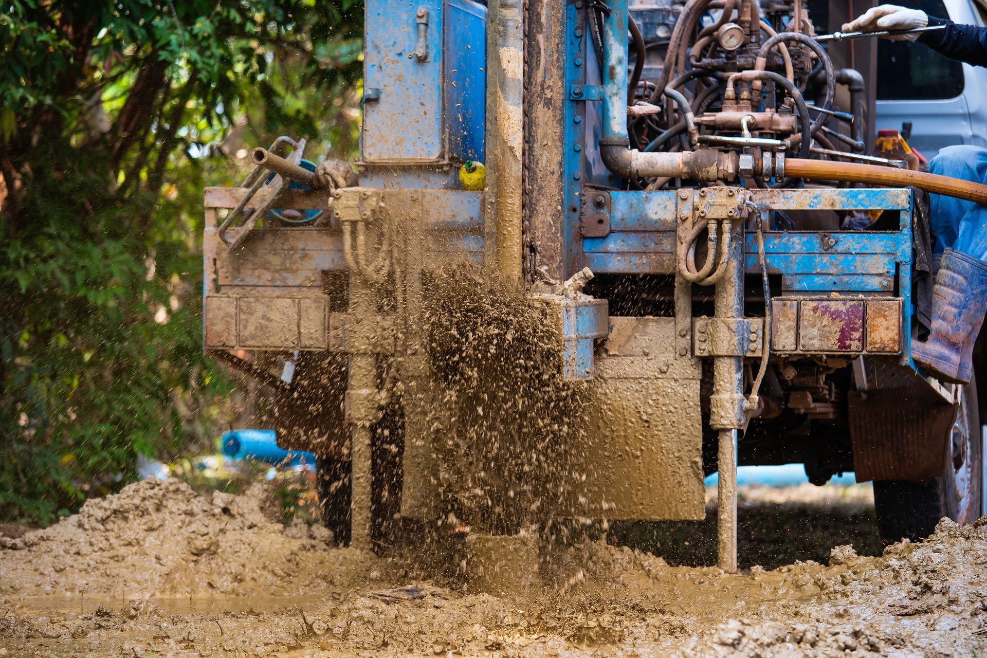 Drilling rig ejecting mud onto the ground, blue machinery in a yard.