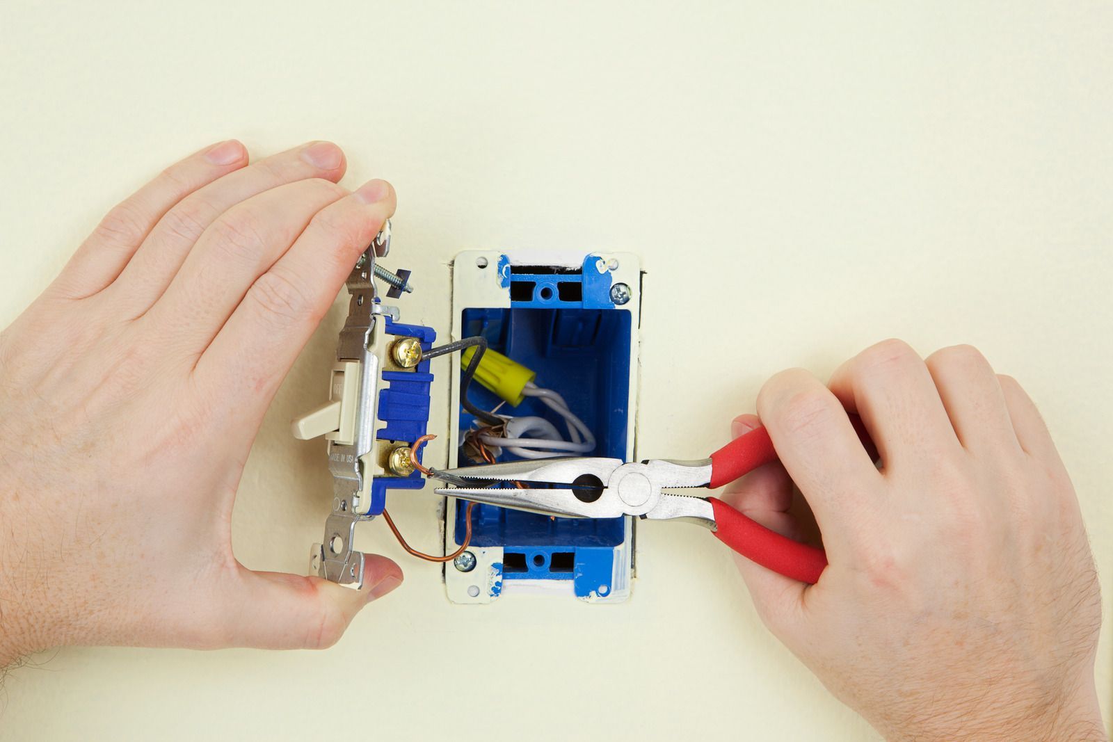 A person is fixing a light switch with a pair of pliers.
