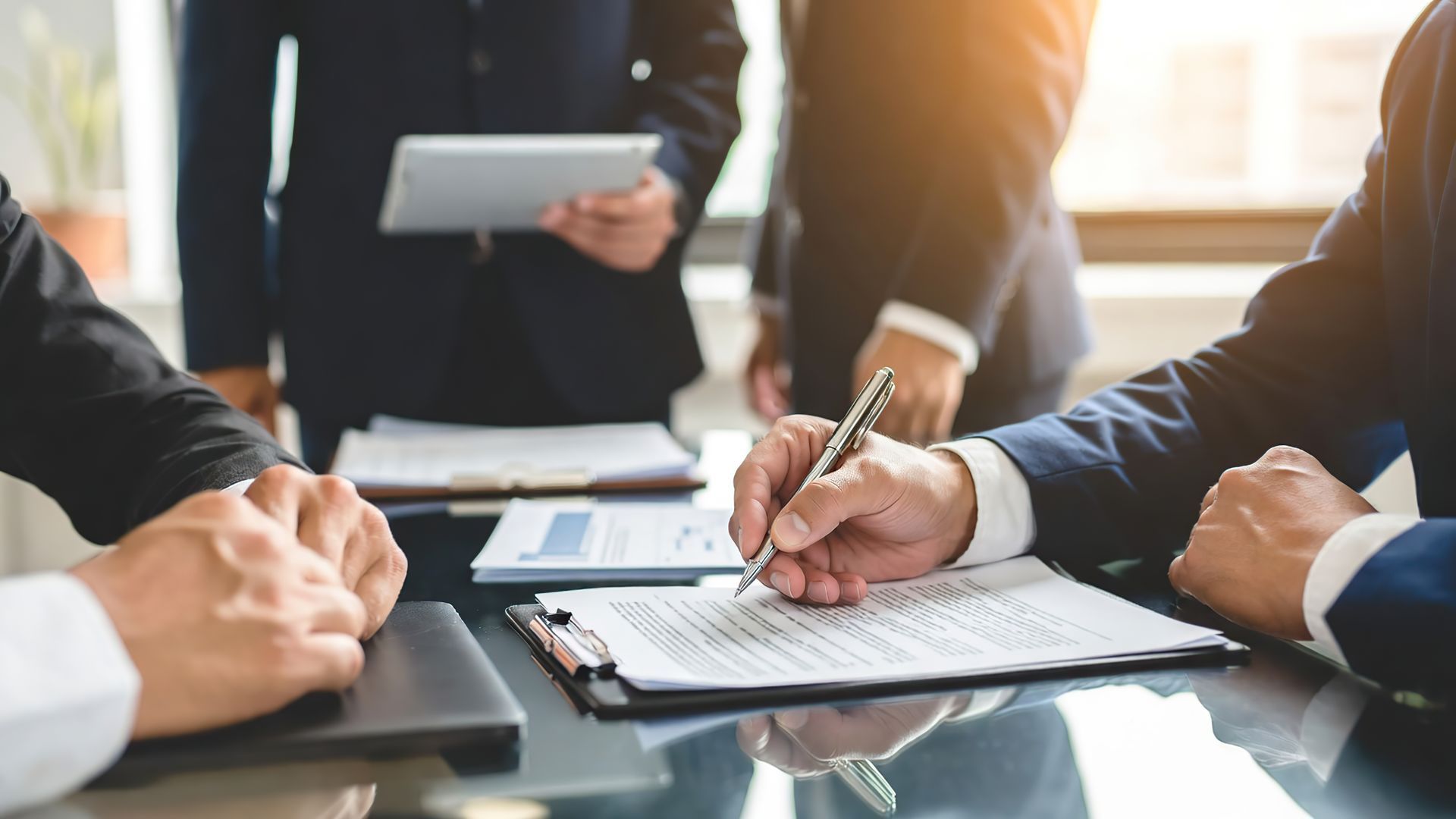 A businessman's hand signing an important official contract during a formal meeting. A businessman's hand signing an important official contract during a formal meeting.
