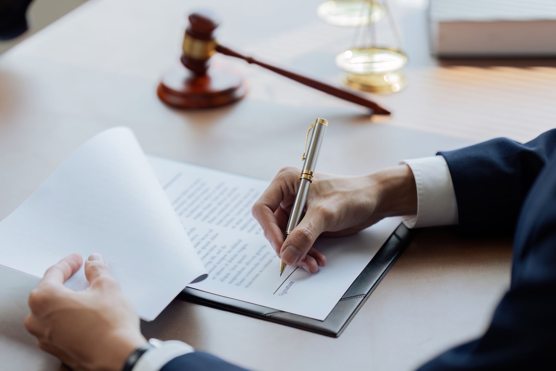 Hand signing a document at a desk with a judge’s gavel in the background