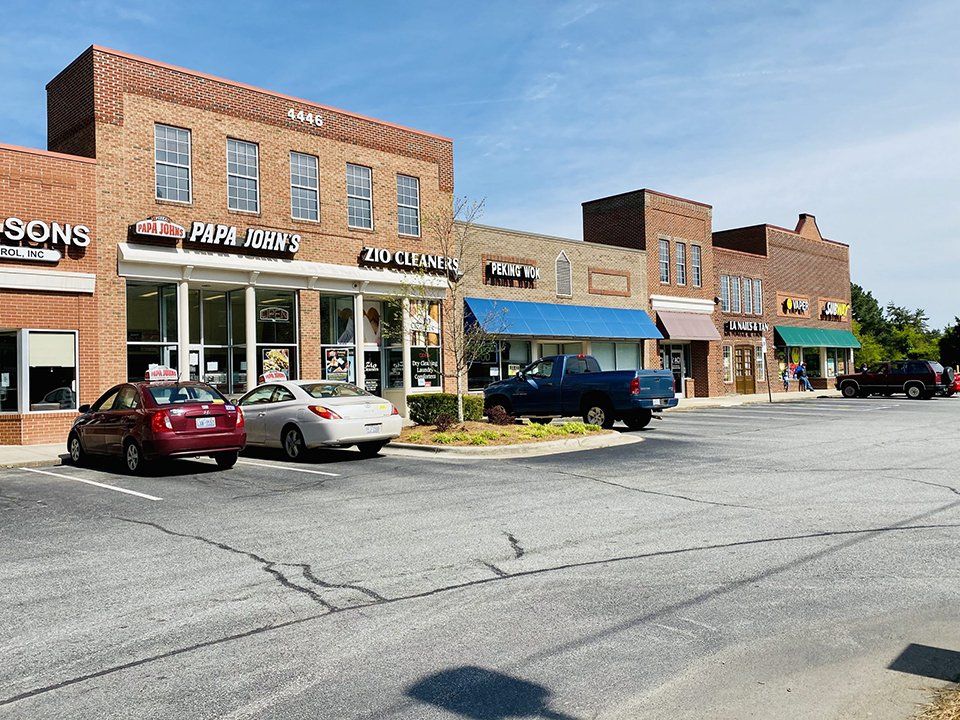 Brick storefronts with businesses, cars parked, sunny day.