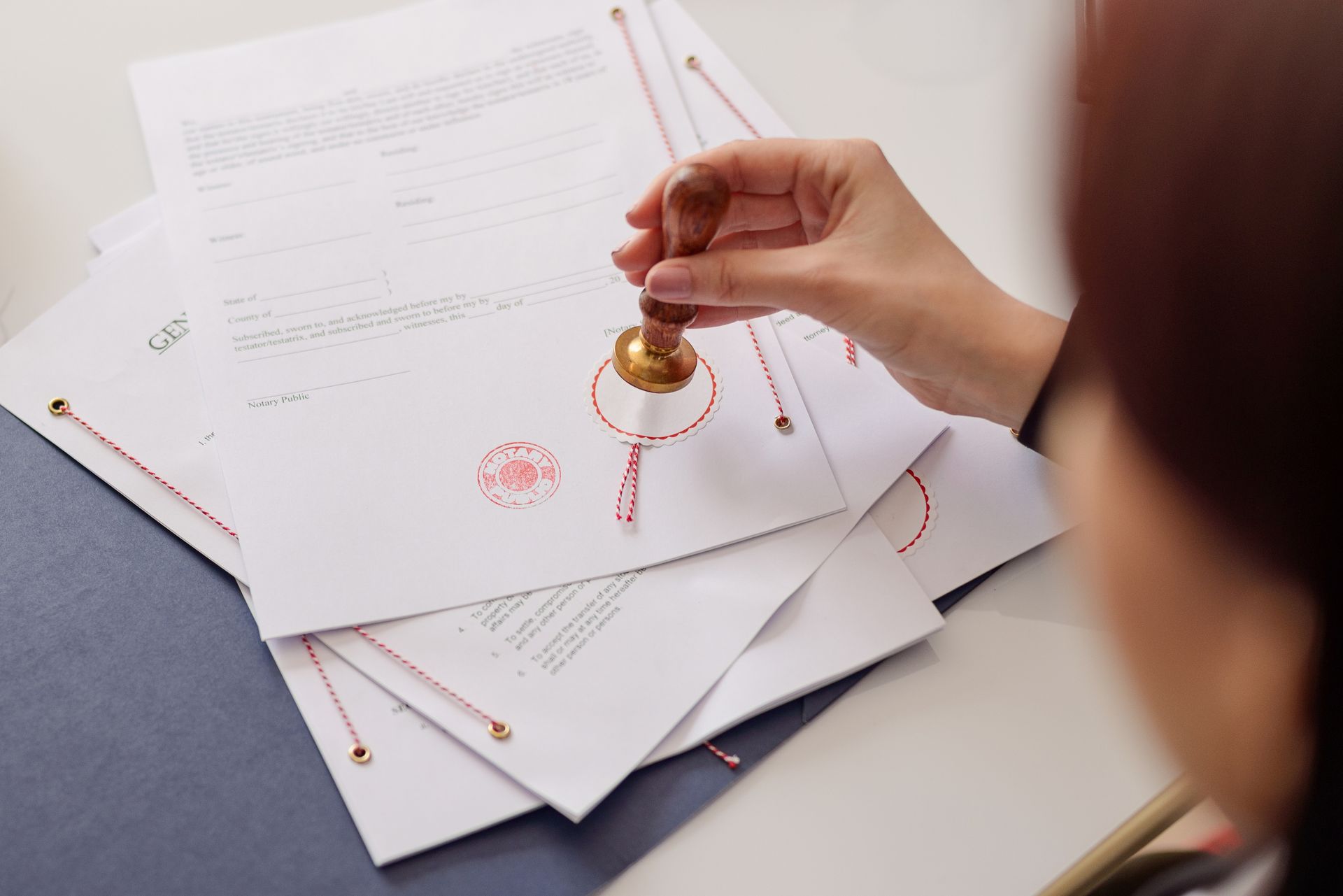 Hand stamping documents with a red seal, several sheets stacked, tied with string.