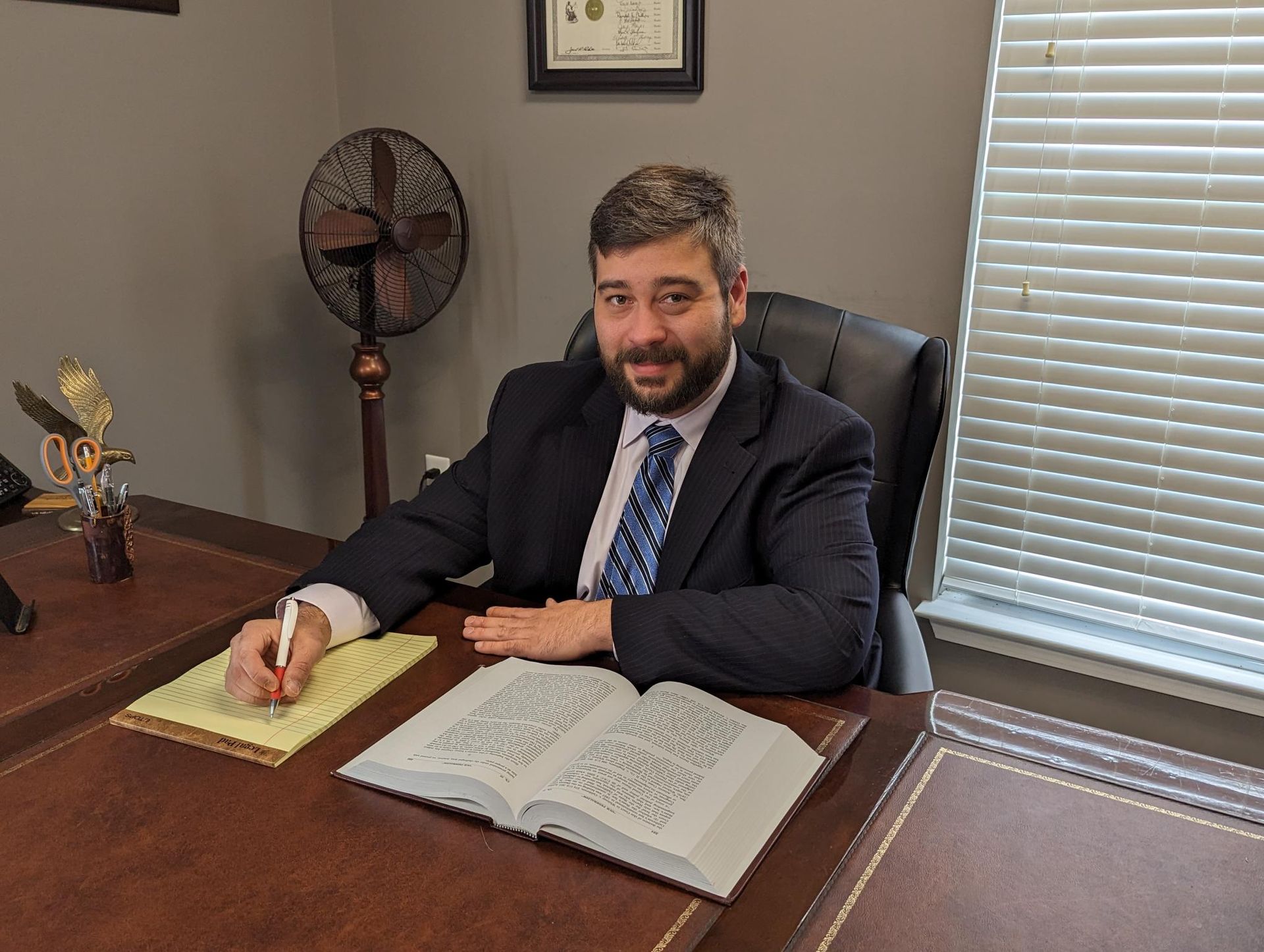 Man in suit at desk, writing. Open book, legal documents. Office setting.