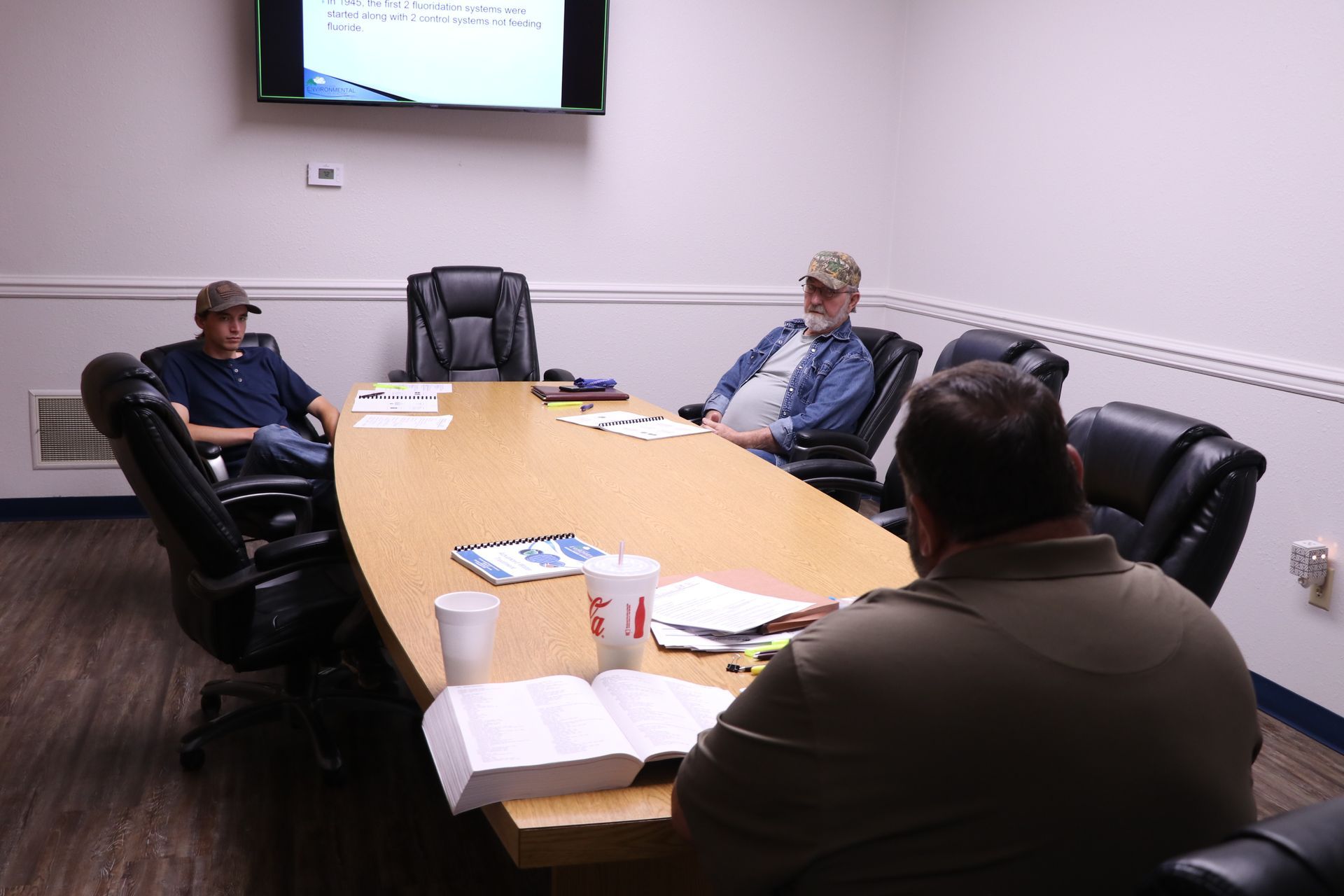 People seated around a conference table in a meeting room, with papers and a wall-mounted screen.