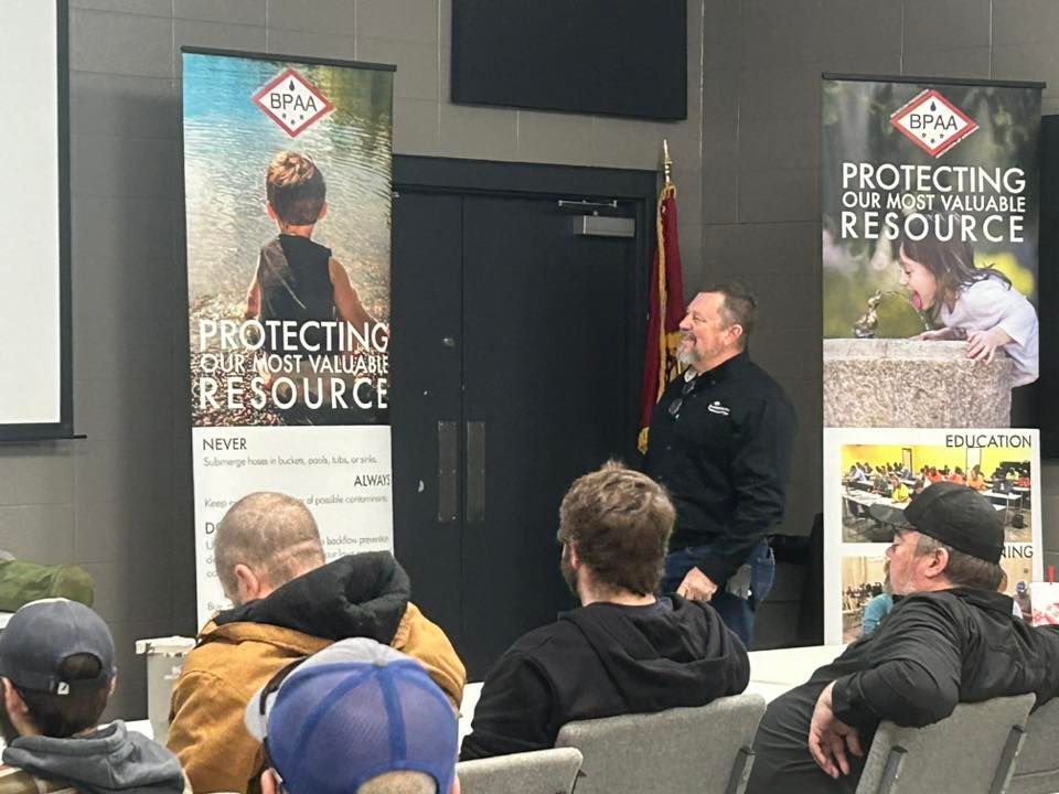 Speaker presenting at a workplace event beside “Protecting Our Resource” banners, with seated attendees facing him.