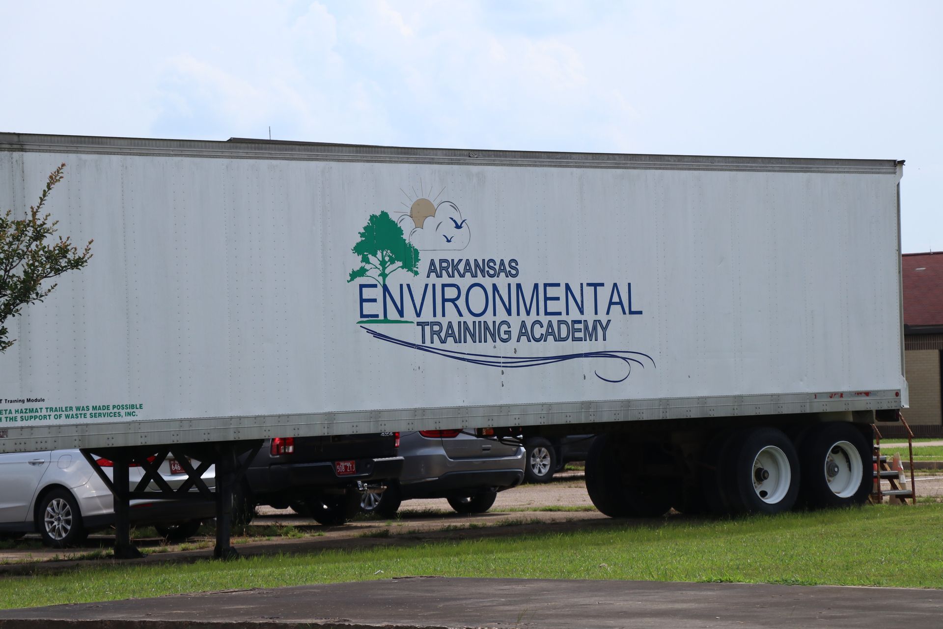 White trailer with Arkansas Environmental Training Academy logo parked on grass near cars and trees