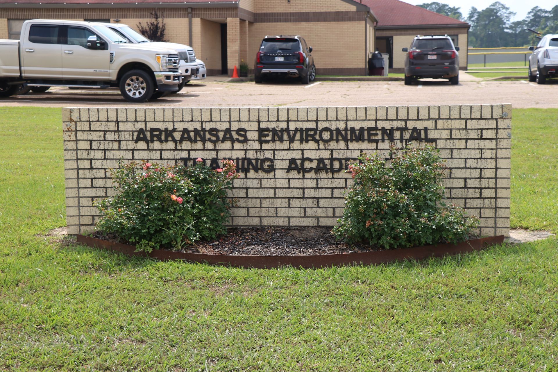 Brick sign for Arkansas Environmental quality office with shrubs in front and parked vehicles behind