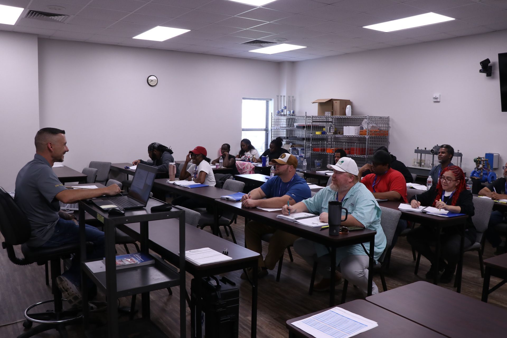 Classroom training session with adults seated at tables, listening to an instructor at the front