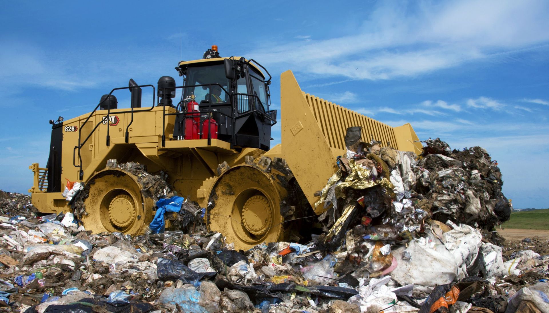 Yellow bulldozer pushing trash in a landfill under a blue sky