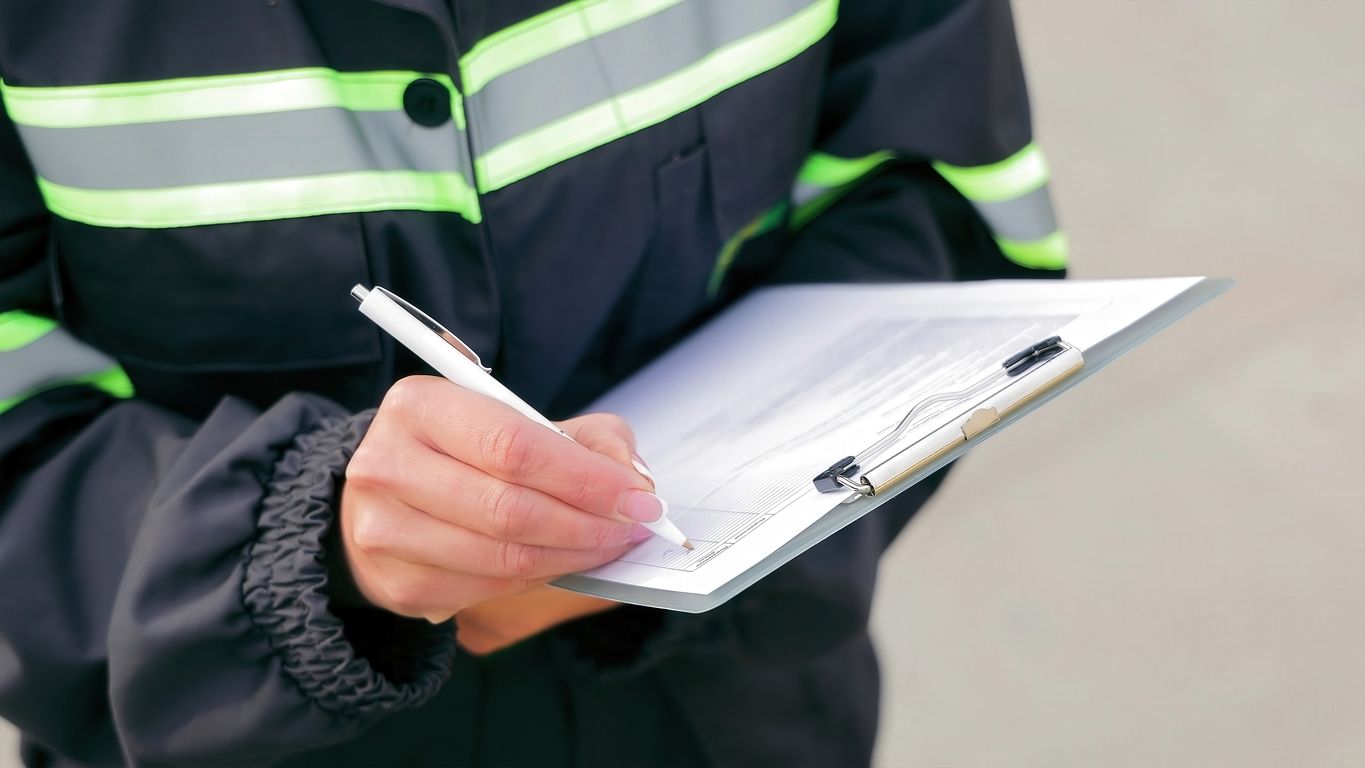 Person in a dark jacket with neon stripes writing on a clipboard