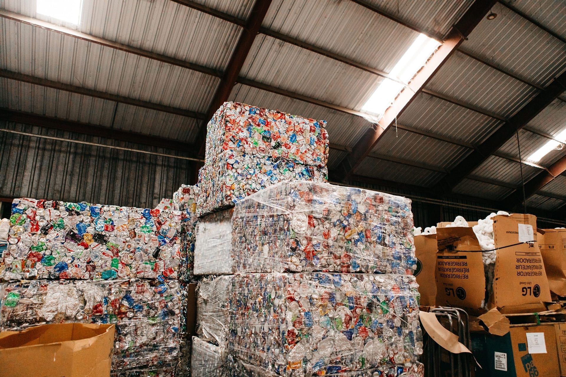 Warehouse stacked with compressed plastic bales and cardboard boxes under a metal roof