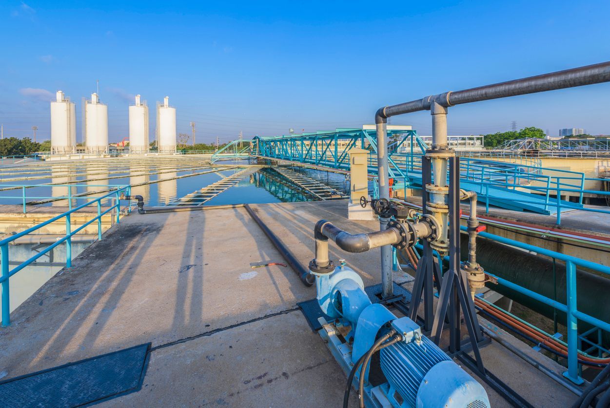Industrial pipes and tanks at a water treatment plant under a clear blue sky