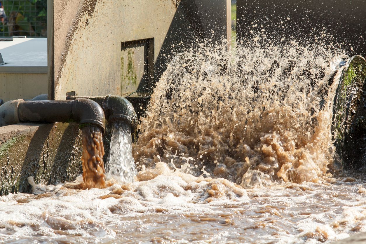 Industrial pipes discharging muddy water, splashing into a flooded basin