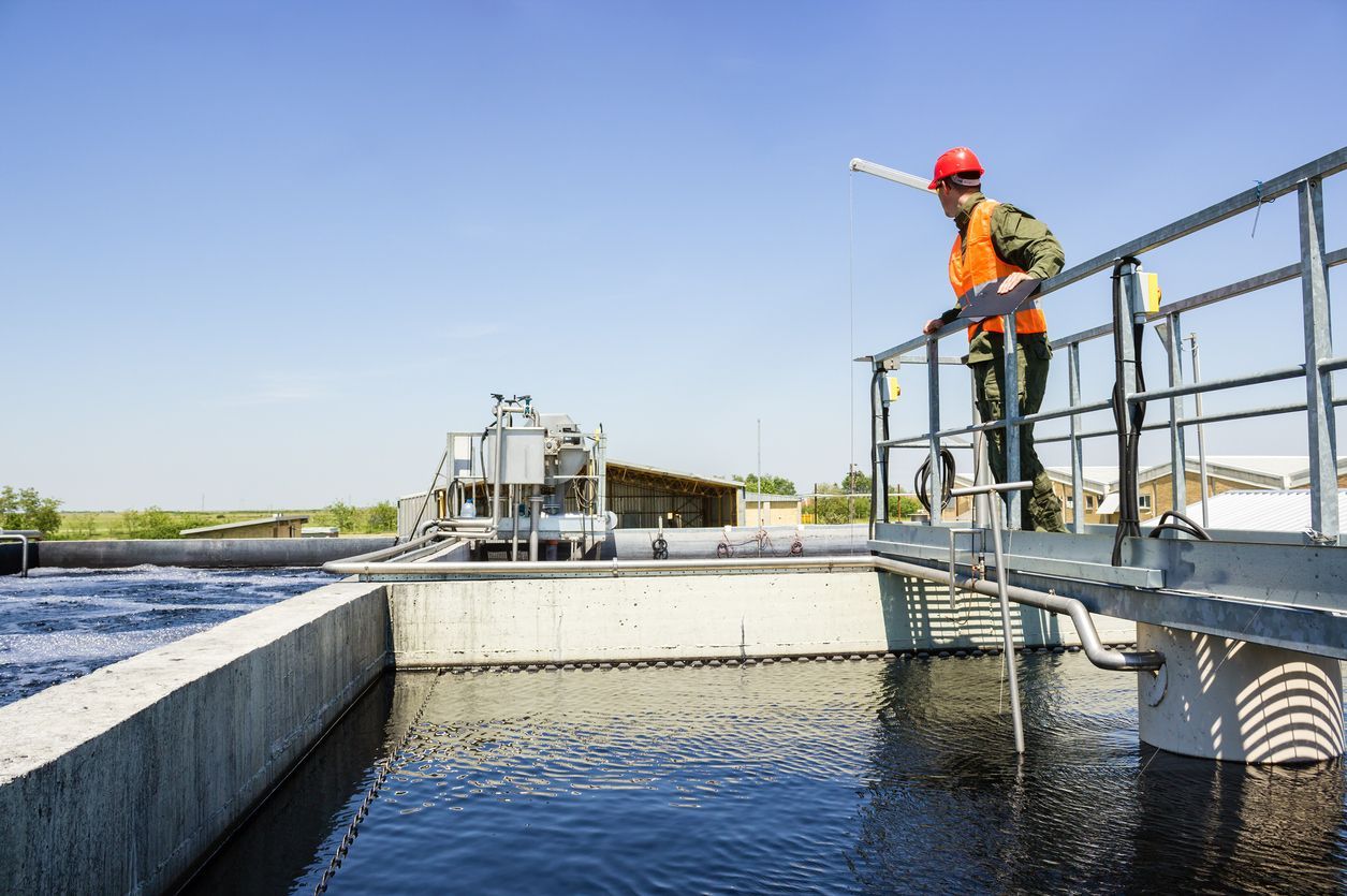 Worker in orange safety gear on a metal platform beside a water treatment basin under a clear sky
