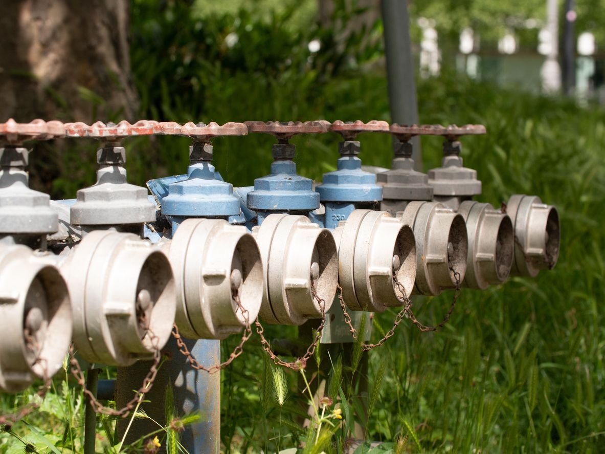 Row of outdoor utility meters with blue caps mounted on a pipe beside grass