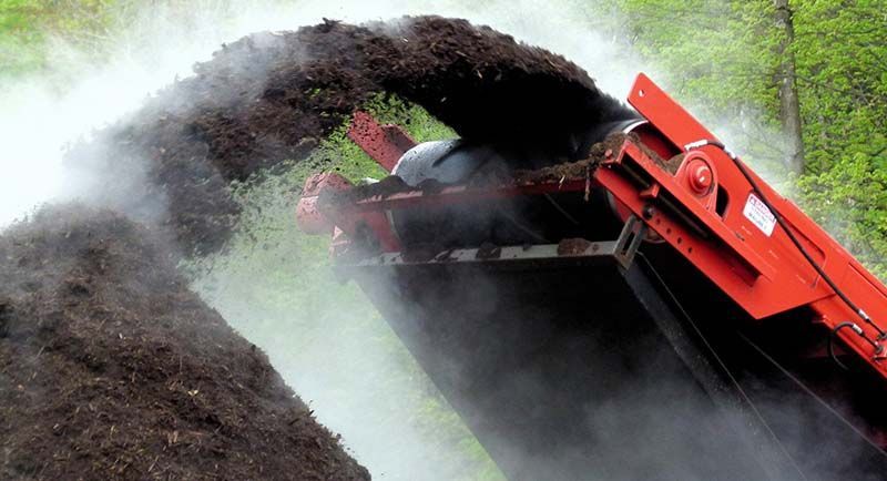 Red excavator dumping dark soil, creating a cloud of dust in an outdoor worksite
