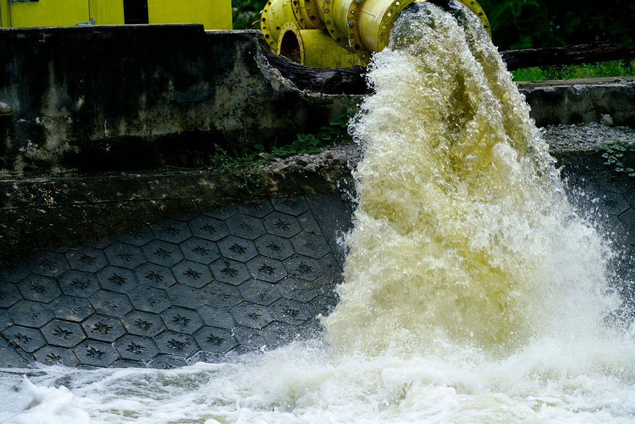 Wastewater pouring from a yellow pipe into a foamy industrial basin