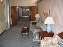 Living room with striped sofa, wooden tables, lamps, and a hallway in the background