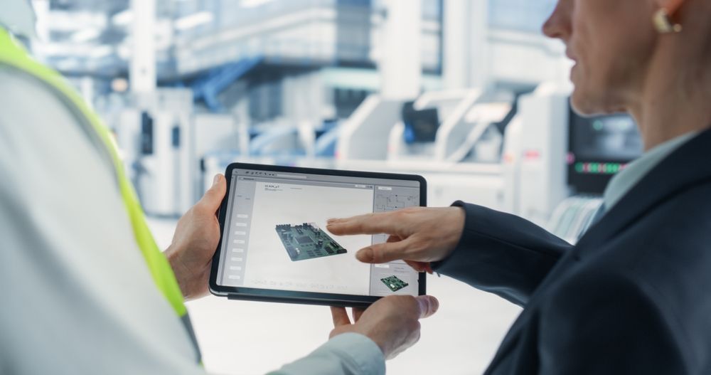 Two people in an office reviewing a tablet showing a floor plan at a worksite.