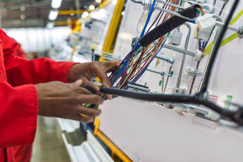 Hands wiring a control panel with colorful cables in an industrial setting