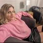 Woman in a pink sweater and black skirt reclining on a couch in a living room.