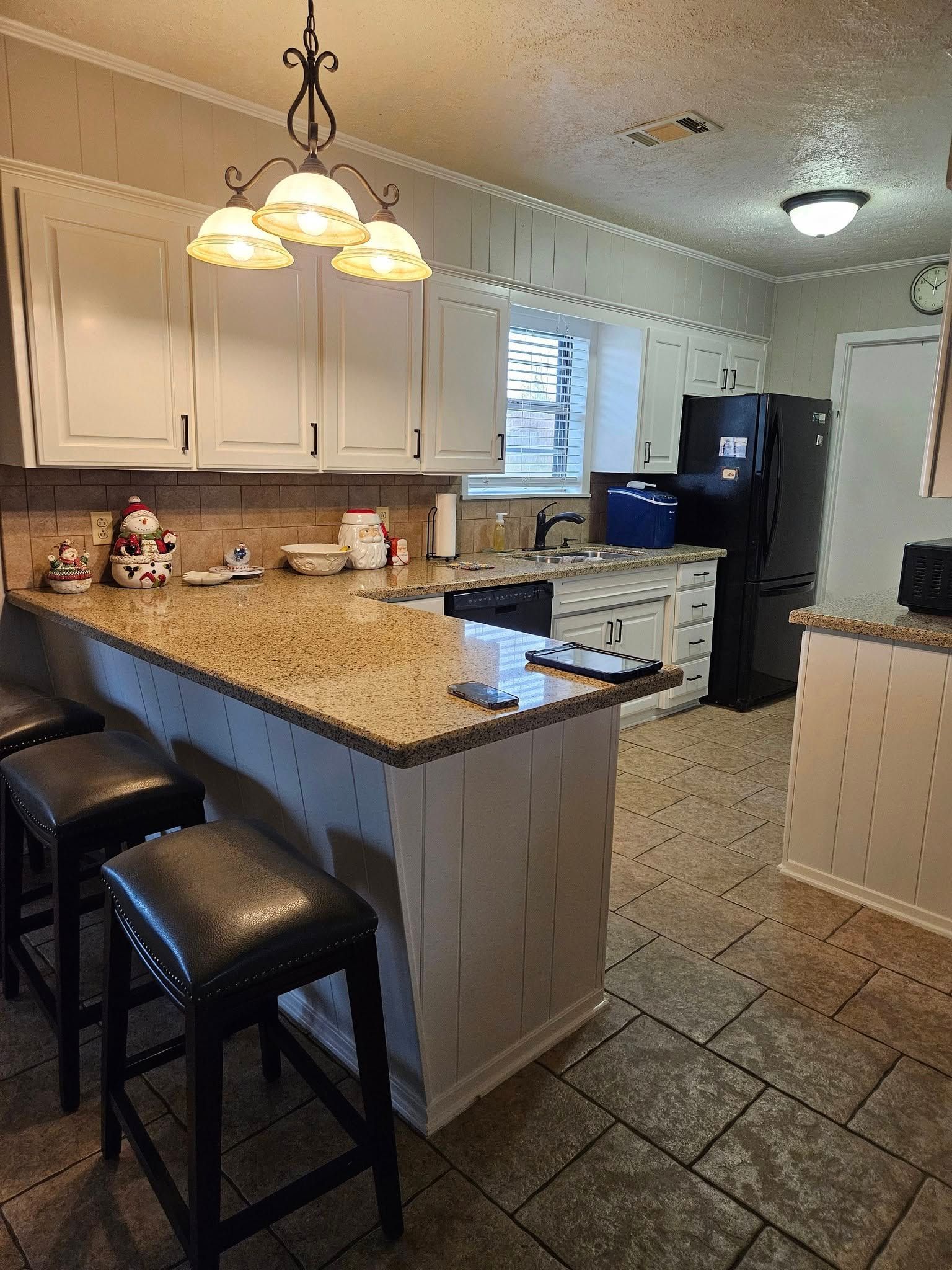 Kitchen with white cabinets, granite countertops, and black stools.