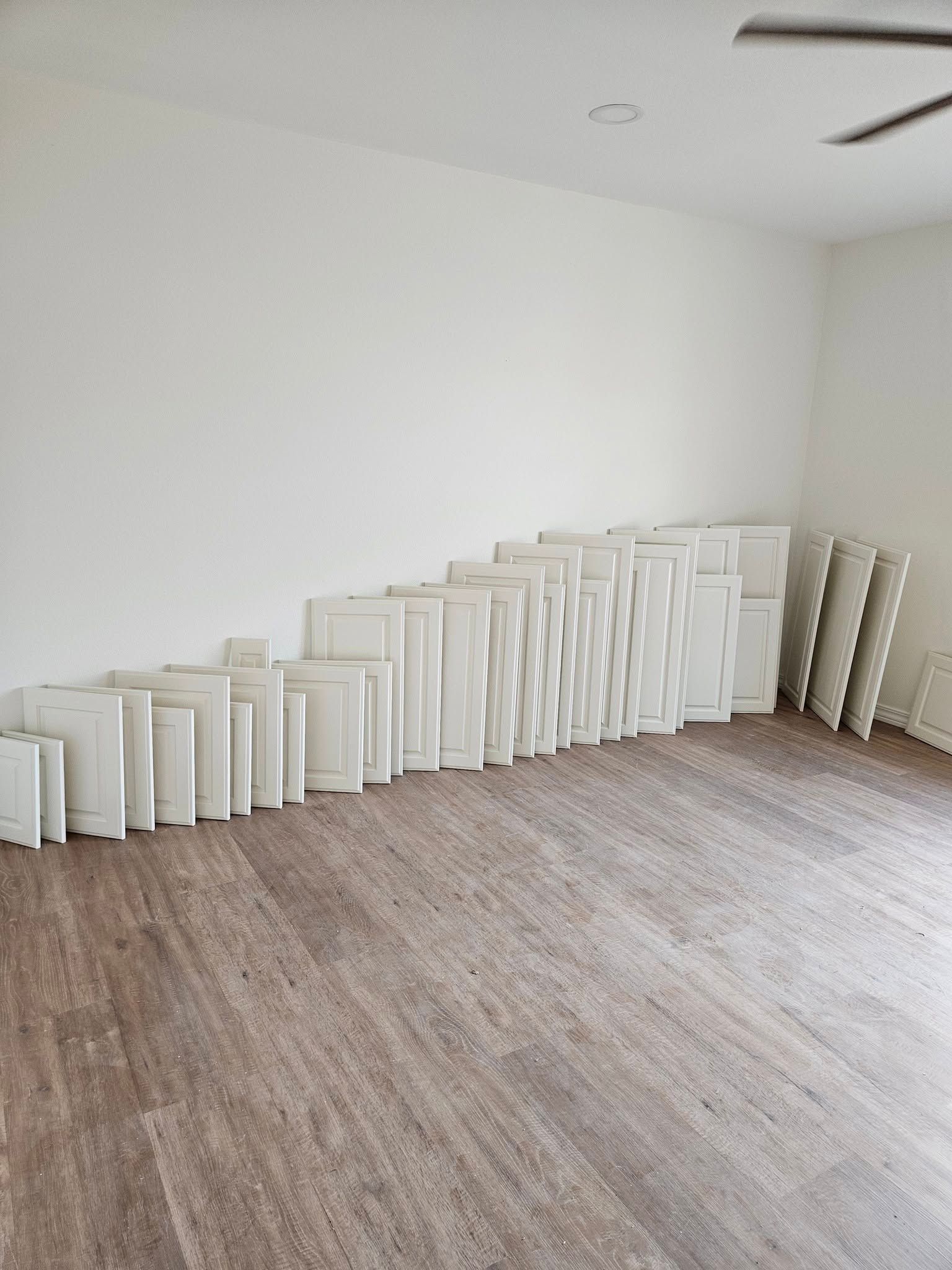 White cabinet doors leaning against a white wall in a room with wood-look flooring.