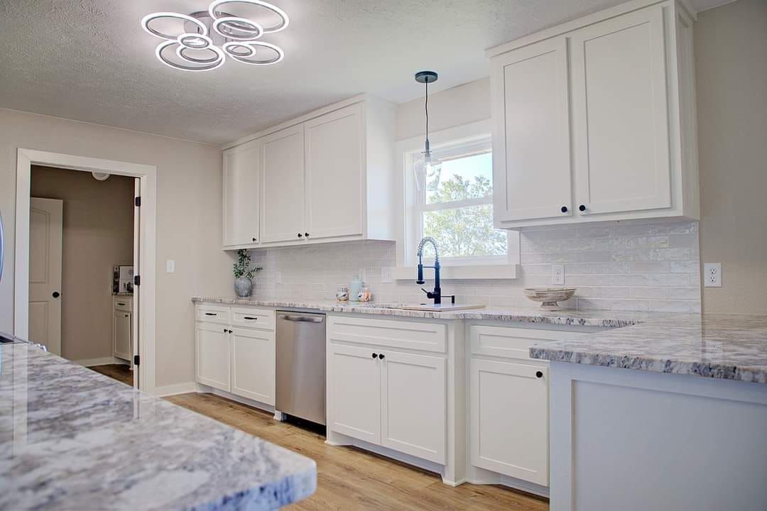 White kitchen with granite countertops, stainless steel appliances, and wood flooring.