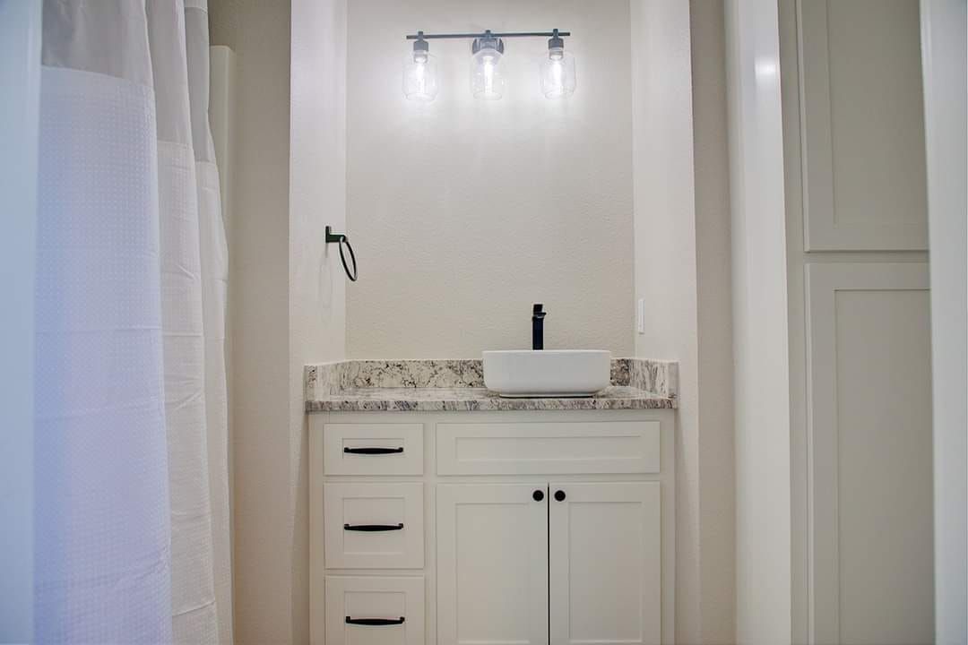 White bathroom with vanity, sink, light fixture, and towel holder.