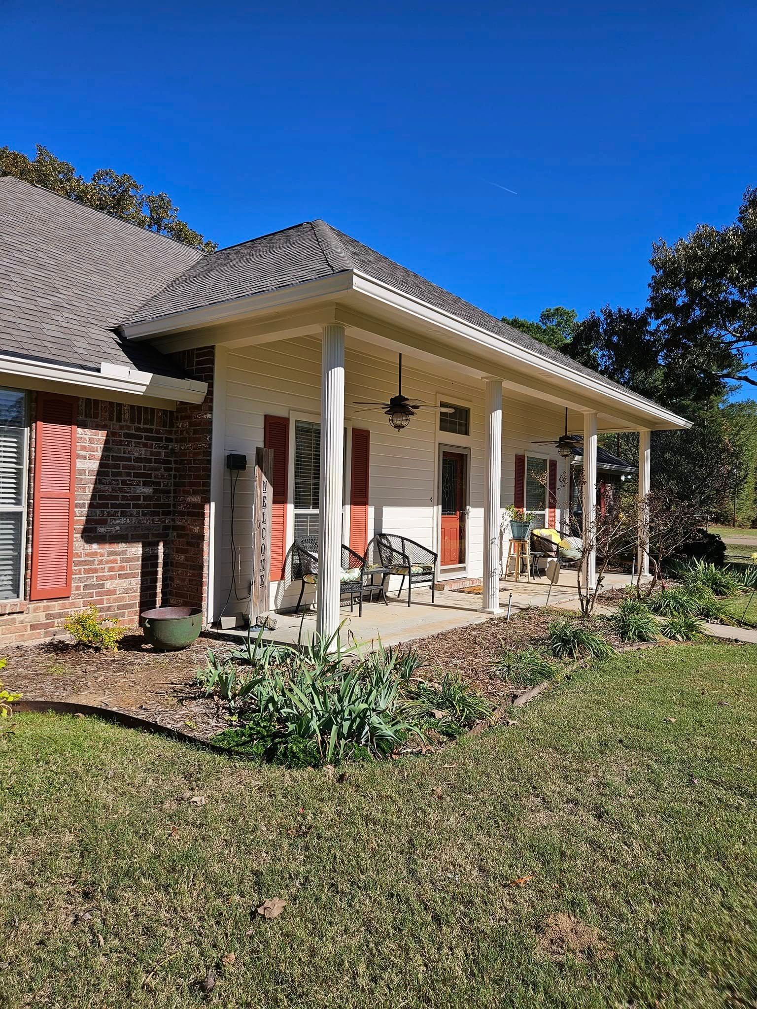 House with a porch and red shutters; brick facade, tan siding, and a grass lawn on a sunny day.