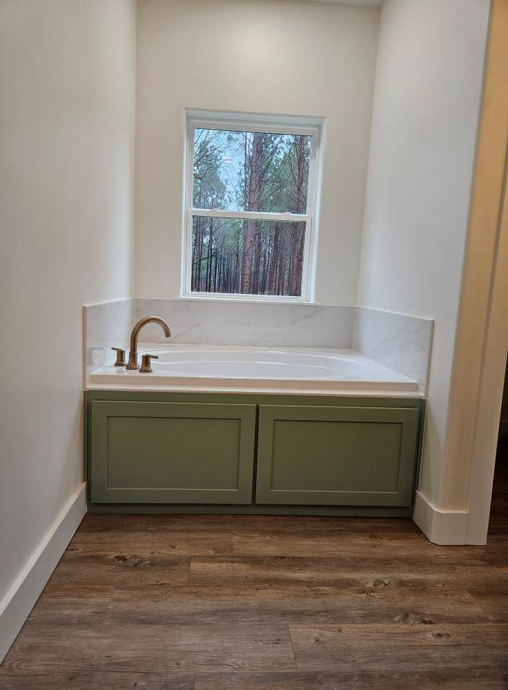 Bathroom with a green cabinet bathtub area under a window, featuring a silver faucet and white marble.