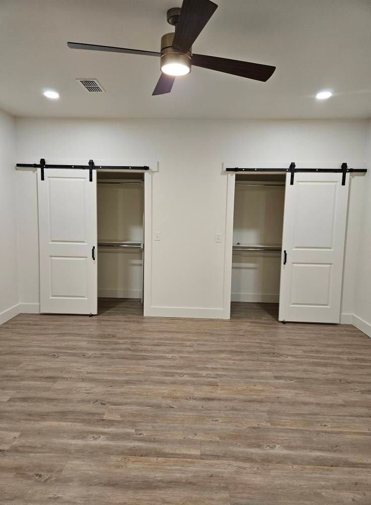 Bedroom with white sliding closet doors, wood floor, and ceiling fan.