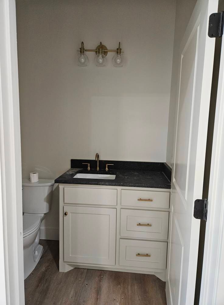 Small bathroom with vanity, toilet, gold light fixture, and beige walls.