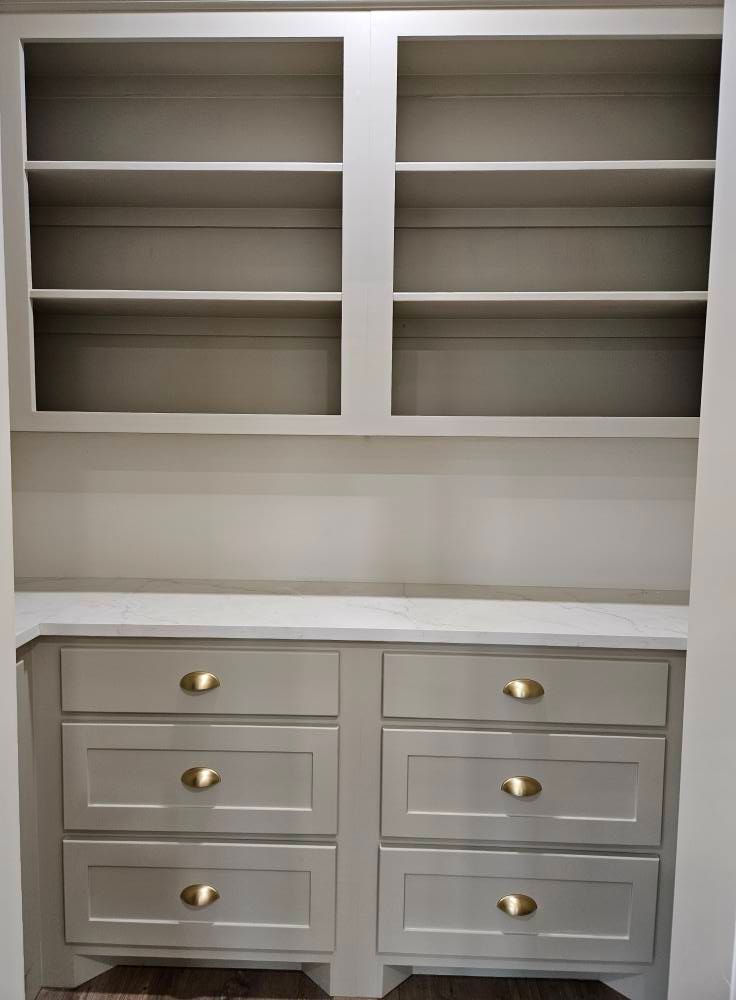 Built-in storage unit with upper shelves and lower drawers; neutral paint with gold hardware.
