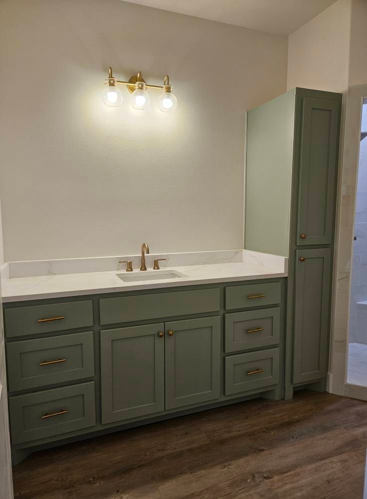 Bathroom with sage green cabinets, gold fixtures, and a white countertop.