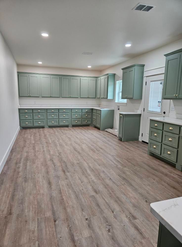 Empty kitchen with sage green cabinets, white countertops, and wood-look flooring.