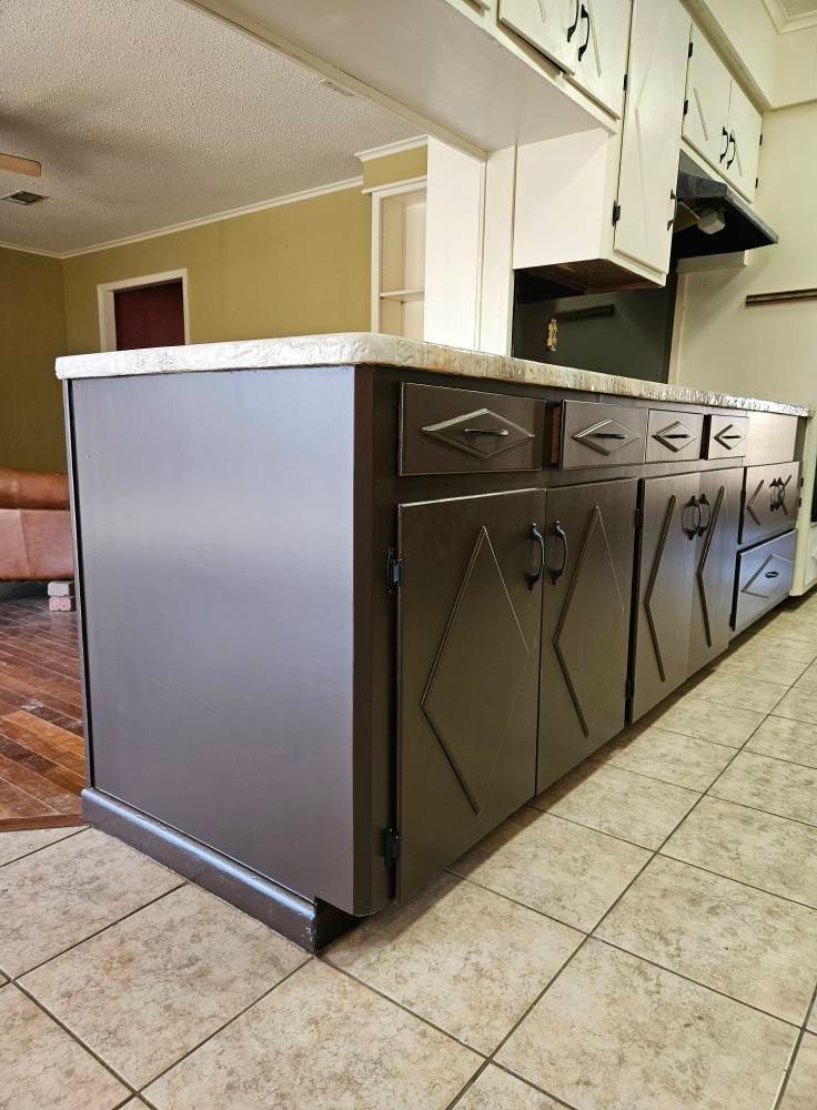 Dark gray kitchen island with a granite countertop, in front of white cabinets.