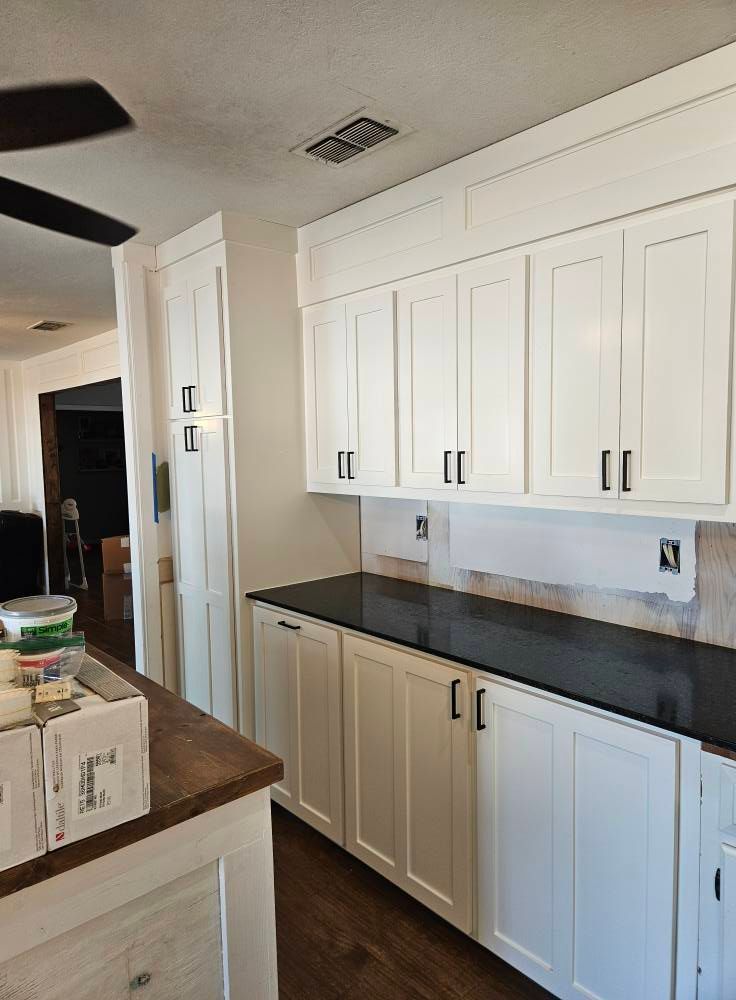 White kitchen cabinets with black countertops and hardware.