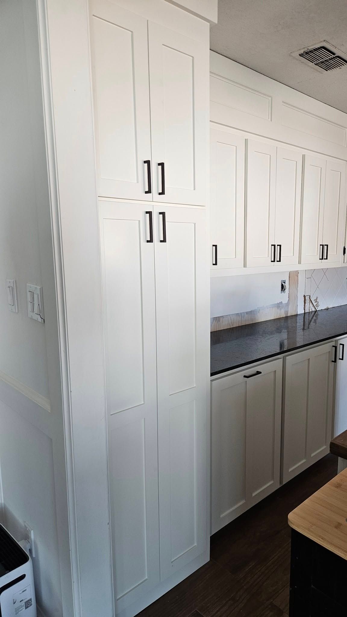 White kitchen cabinets with black hardware; part of a kitchen.