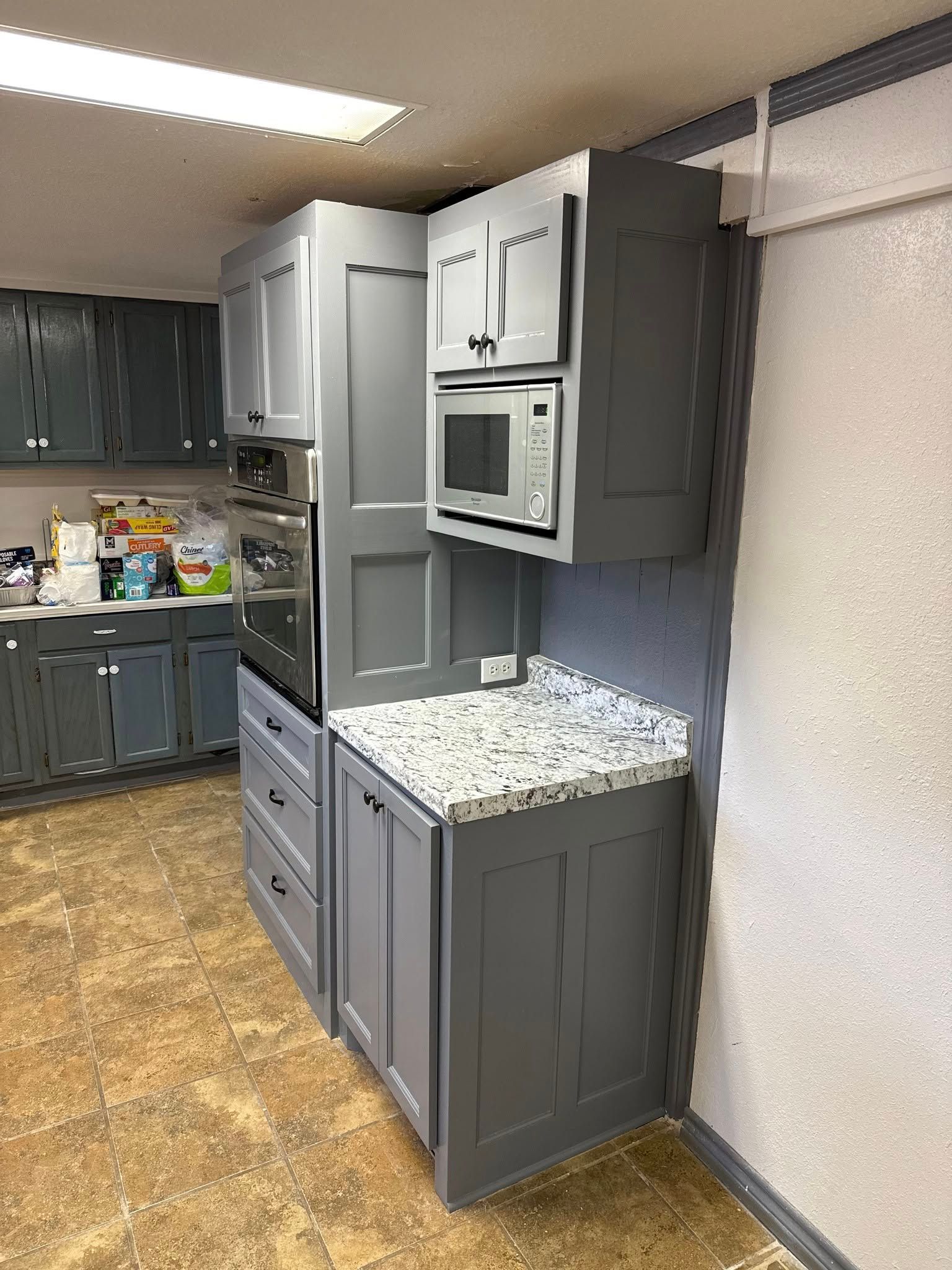 Gray kitchen cabinets and appliances with granite countertop.