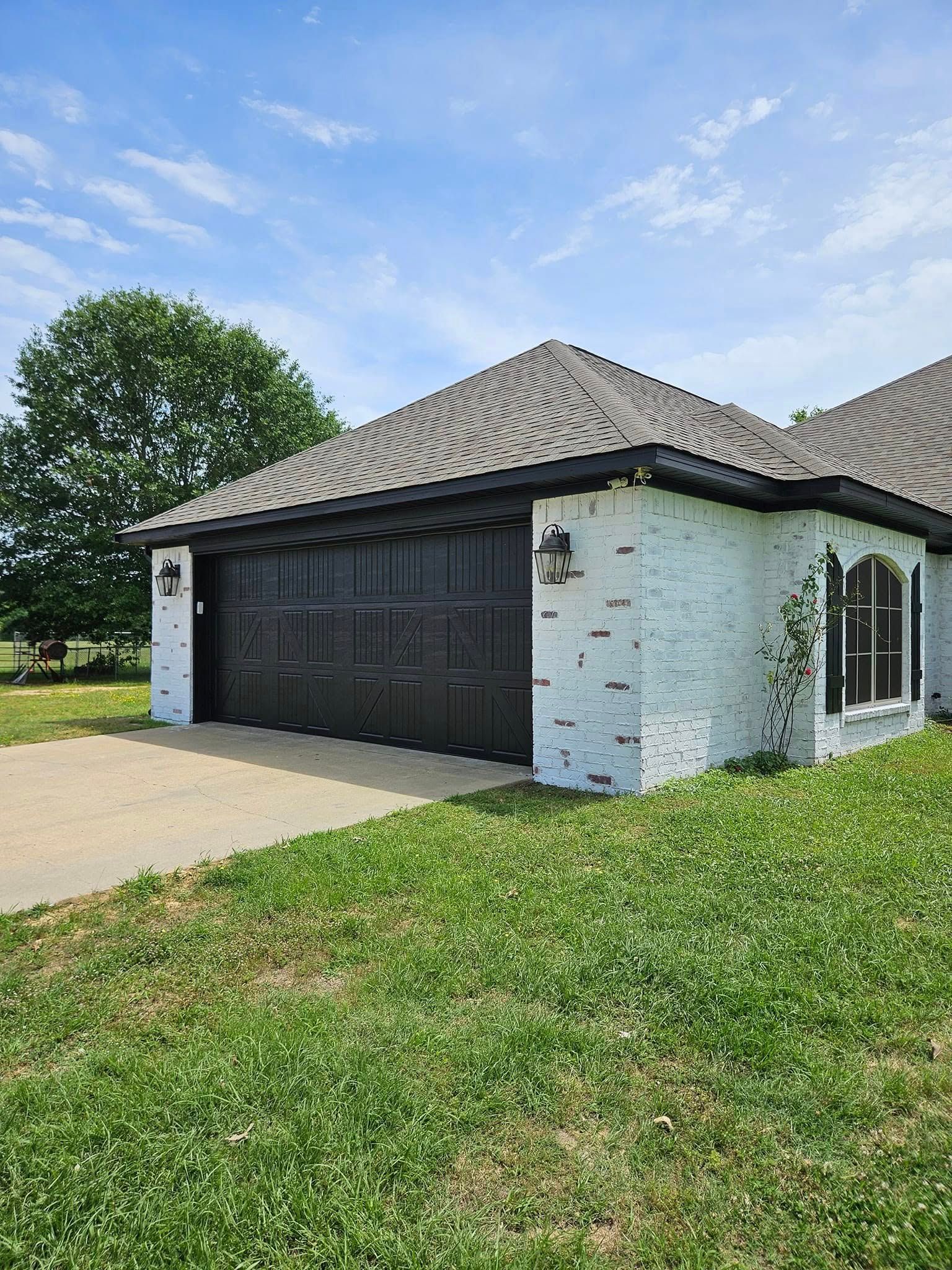 White brick garage with black door, roof, and trim, green grass, and blue sky.