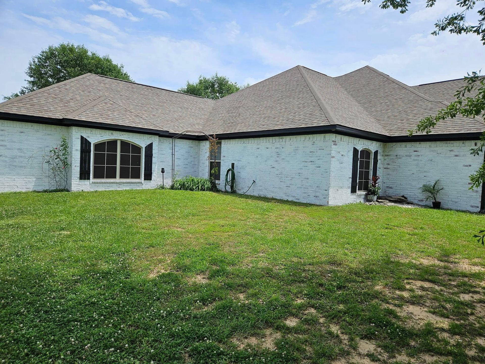 White brick house with gray roof and black shutters, set on a green lawn.