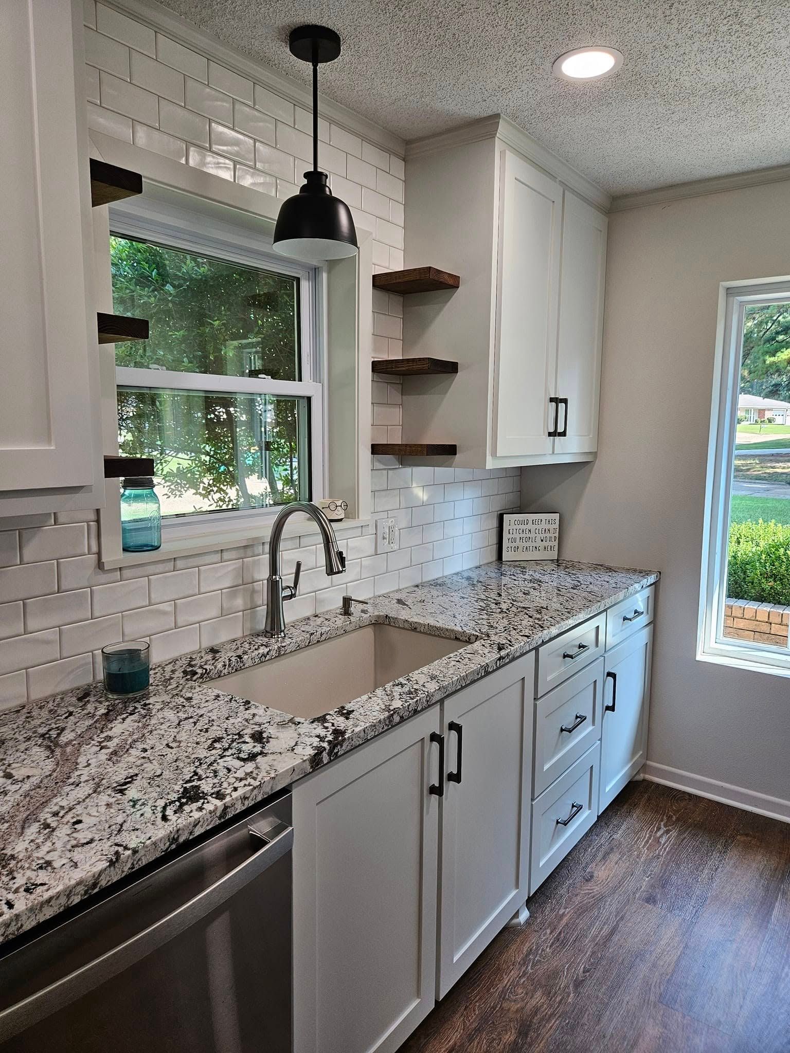 White kitchen with granite countertops, subway tile backsplash, and dark cabinet hardware; a window is visible.